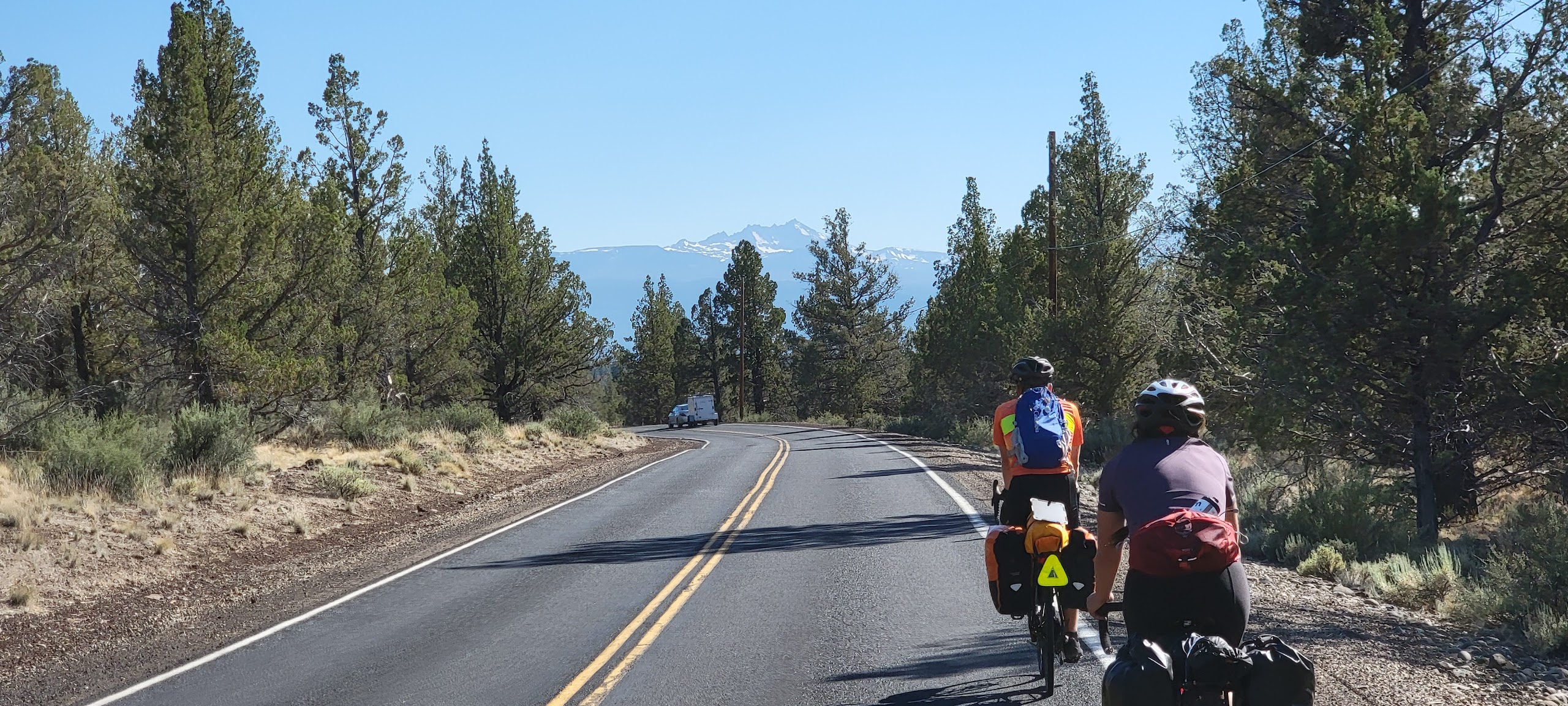 5 people pose on the back of a truck, with bikes in the back. They are all smiling and appear to be having a great time.